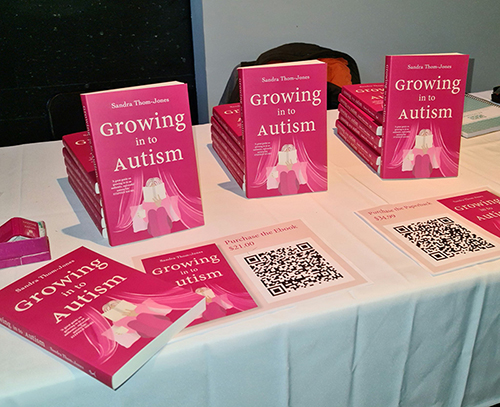  Several pink books with the title 'Growing in to Autism' on a table covered by a white tablecloth