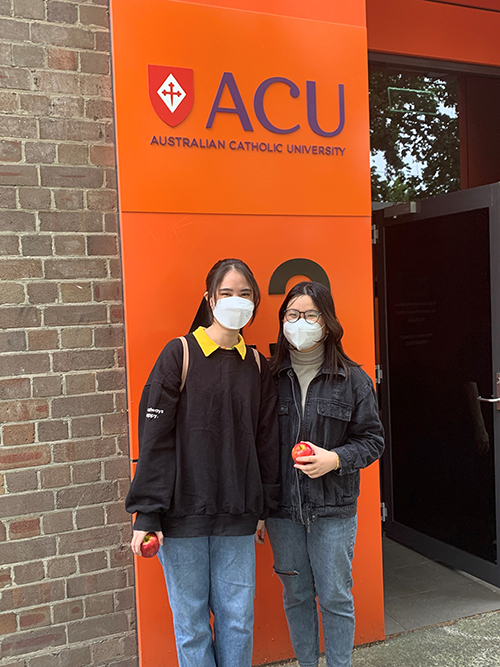  Two female students stand in front of an orange sign that says ACU