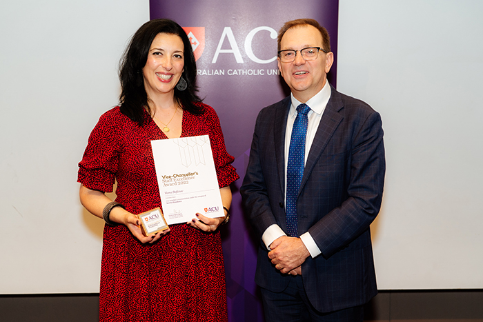  Woman with dark  shoulder length hair in a red dress holding a certificate and plaque with a man in a dark suit and glasses