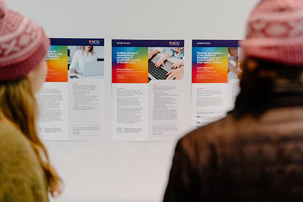  Three posts about autism research on a wall with two people blurred in the foreground